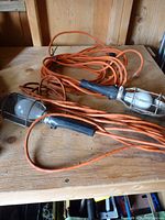 Two handheld trouble lights with orange cords on wooden surface