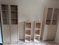 Five matching light wood IKEA pieces arranged against wall; tall cabinets with doors, two small bookcases at center
