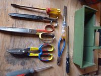 Assorted scissors, pliers, screwdrivers, files, tin snips and green toolbox tray on wooden surface