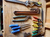 Board holding assorted hand tools including wrench, pipe wrench, pliers, screwdrivers, files, aviation snips, cable ties, hammer head