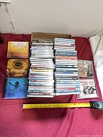 Full lot view with stacks of jewel-cased DVDs and tape measure for scale