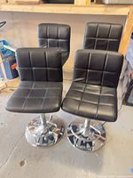 Four black faux leather bar stools grouped together