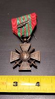 Front view showing bronze cross with Marianne medallion, crossed swords, ribbon, and palm device, tape for scale