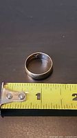 Gold band ring beside tape measure showing roughly 2 cm diameter, interior hallmarks visible