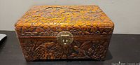 Front view of carved wood jewelry box with latch showing bird and floral carvings