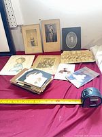 Entire lot laid out on table showing mounted portraits, class photo, coloured print, and stack of snapshots with tape measure for scale
