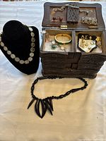 Full lot showing carved wooden jewelry chest with assorted pieces, coin necklace on display, black bead necklace on table