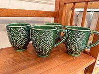 Four green Bordallo Pinheiro pineapple mugs on wood shelf