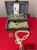 Overall view of open jewelry box showing contents including seed pearl necklace and brooch