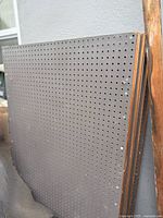 Stack of grey pegboard panels leaning against wall