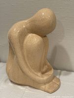 Front view of beige speckled ceramic seated figure sculpture