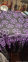 Overall view of black wrap scarf draped, showing purple pentacles and fringe