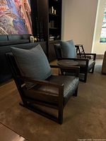 Two identical black leather lounge chairs with blue pillows shown side by side