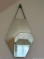 Front view of asymmetrical wall mirror hanging by chromed strap