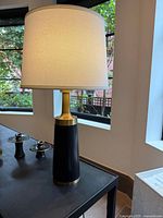 Close view of one lamp highlighting brass neck, black base and white shade