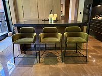 Three matching green velvet CB2 counter stools front view under kitchen island