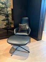 Front view of black leather Zanotta Kent lounge chair and ottoman on graphite swivel bases