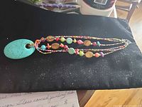 Full view of three-strand beaded necklace with turquoise donut pendant