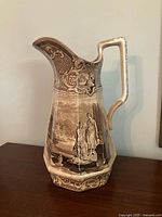 Front view of brown transferware pitcher showing classical scene and ornate design
