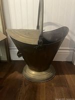 Side view of brass coal scuttle showing bail handle and pedestal base