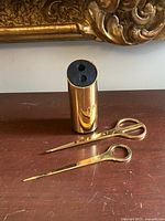 Cylindrical brass holder, letter opener and scissors lying flat