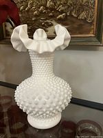 Full view of white hobnail milk glass vase on shelf