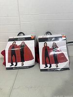 Two packaged red hooded capes on table