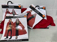 Four packaged red hooded capes on hangers