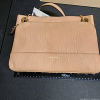 Front view of tan Calvin Klein handbag next to ruler