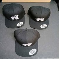 Three identical black Los Buenosi snapback hats, lion logo visible