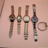 Five wristwatches displayed on pink background