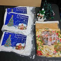 Full lot showing three fake snow packages, string lights bundle, tablecloth, snowman figure