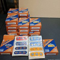 Stack of multiple unopened Cure NBA bandage boxes with two open sheets showing bandage designs