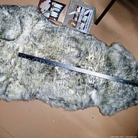 Full view of grey sheepskin rug with measuring tape showing length and storage bag with guide adjacent
