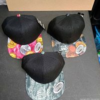 Overview of three black baseball caps with patterned brims and tags