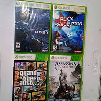 Front view of four Xbox 360 game cases: Halo 3 ODST, Rock Revolution, Grand Theft Auto V, Assassin's Creed III
