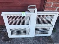 Full view of expandable white gate leaning against wall