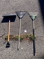 Three long-handled garden tools laid out on pavement