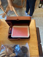 Open wooden cribbage box showing playing cards and coloured pegs; plastic bag of wooden discs visible