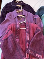 Three jackets in purple and rose tones on hangers