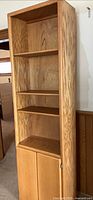 Full view of tall oak bookcase cabinet showing open shelves and lower doors