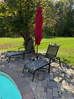 Two black metal lounge chairs and red umbrella by pool
