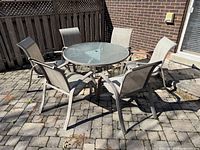Round glass-top patio table with six sling chairs on stone patio