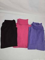 Three folded sweaters in brown, pink, purple