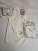 Full set showing sleep sack, bib, bath mitt in packaging, and small container