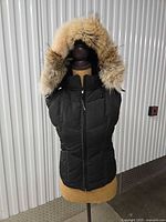 Front view of black Canada Goose down vest with fur-trimmed hood on mannequin