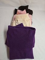 Stack of four folded sweaters showing colors and knit texture