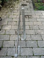 Three silver metal drapery rails with glass finials laid on stone patio