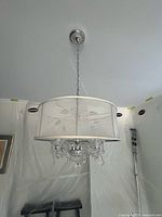 Full view of pendant light hanging from ceiling, showing drum shade, chain, canopy, and crystal drops