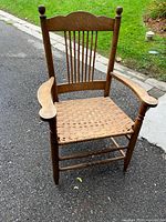 Front view of wooden armchair showing spindle back, curved arms, woven rattan seat